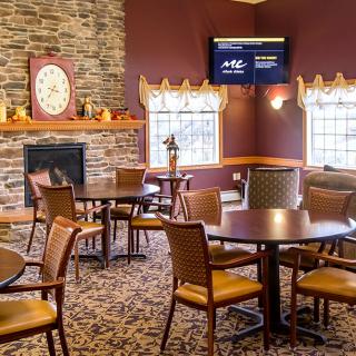 A cozy restaurant interior featuring a fireplace, several tables and chairs, and a wall-mounted television.