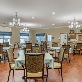 A spacious dining room with neatly arranged tables and chairs, accented by chandeliers and wooden flooring.