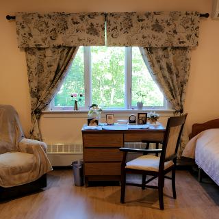 A cozy bedroom with floral curtains, a desk by the window, and comfortable seating.
