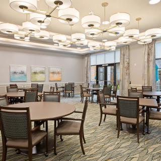 A spacious dining room with round tables and cushioned chairs, adorned with modern chandeliers and artwork on the walls.