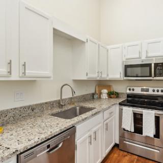 A sleek and modern kitchen featuring white cabinetry and stainless steel appliances, complemented by a granite countertop.