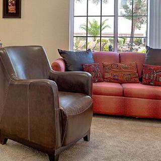 A cozy living room featuring a leather chair and a red sofa, with a large window letting in natural light.