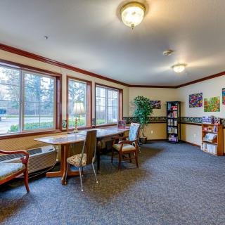 A cozy interior room featuring a large table, several chairs, and a bookshelf with ample natural light from multiple windows.