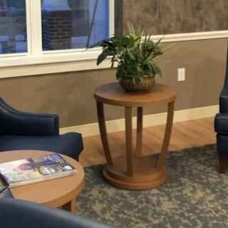 A cozy waiting room with a round wooden table, chairs, and a potted plant.