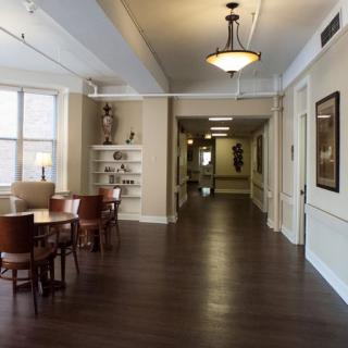A well-lit hallway with a small dining area featuring tables and chairs, hardwood flooring, and decorative lighting.
