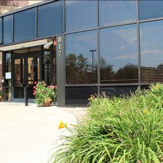A building entrance with large glass windows surrounded by greenery.