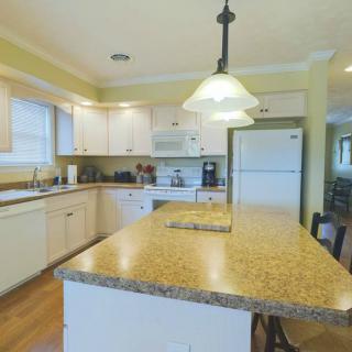 A modern kitchen with a central island, featuring white cabinetry and a well-lit interior.