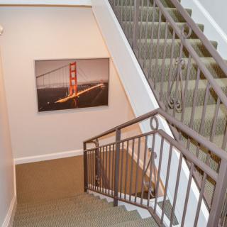 A staircase with carpeted steps and metal handrails, featuring artwork of a bridge on the wall.