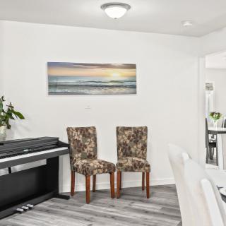 A dining area featuring a piano, two patterned chairs, and a seascape wall art.