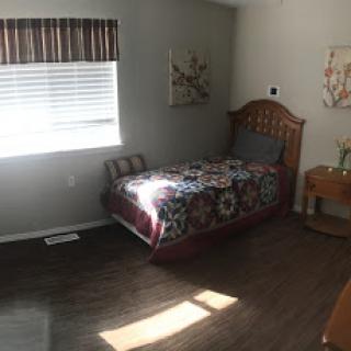 A cozy bedroom featuring a bed with colorful bedding, wooden furniture, and a bright window allowing natural light.