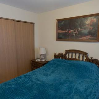 A cozy bedroom featuring a wooden bed with teal bedding, a bedside lamp, and a painting on the wall.