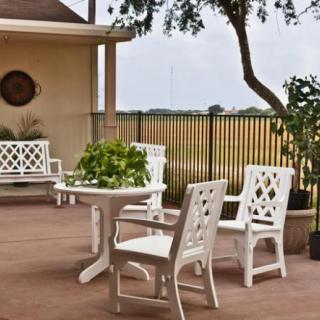 A cozy patio with white outdoor furniture and a potted plant in a garden setting.