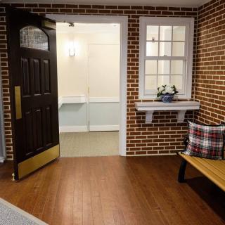 A cozy interior space with a brick wall, open door, and wooden bench adorned with cushions.