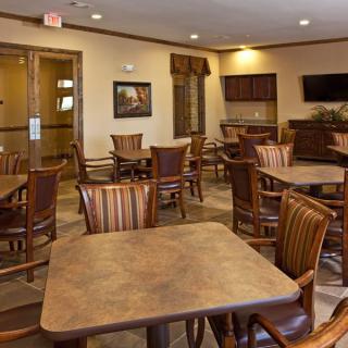 An empty dining area with wooden tables and chairs, featuring a television on the wall.