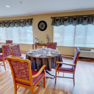 A cozy dining room setup with a round table and upholstered chairs near large windows.
