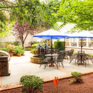 A scenic patio area with tables and chairs under blue umbrellas, surrounded by lush greenery.