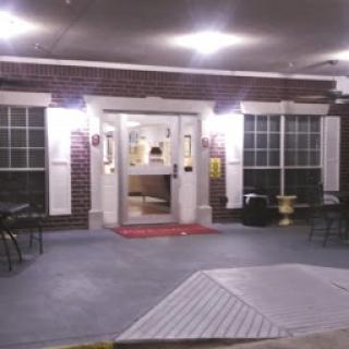A well-lit entrance to a building at night, featuring large windows and outdoor seating.