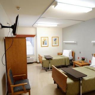A hospital room with two beds, a television, and chairs.