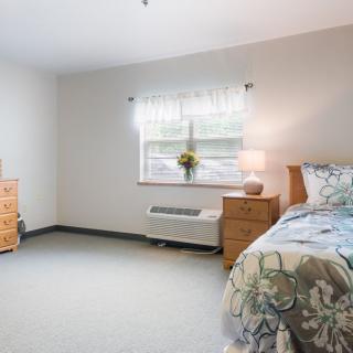 A minimalist bedroom with a bed, dresser, and window with light coming through.
