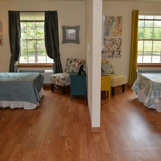 A cozy bedroom with twin beds separated by a partition and featuring wooden floors and large windows.