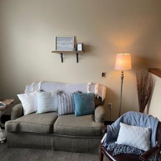 A cozy living room with a sofa, cushions, lamp, and decorative shelf.