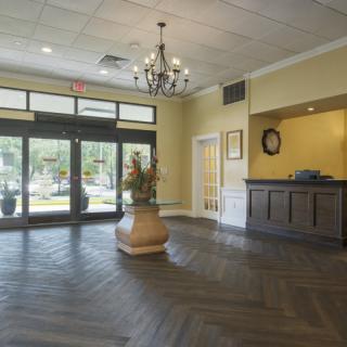 A spacious hotel lobby with a chandelier, wooden floors, and a welcoming front desk.