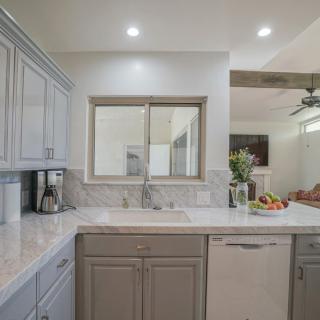 A modern kitchen interior with neutral tones, featuring sleek cabinets, a countertop with a fruit bowl, and a view into the adjacent living area.