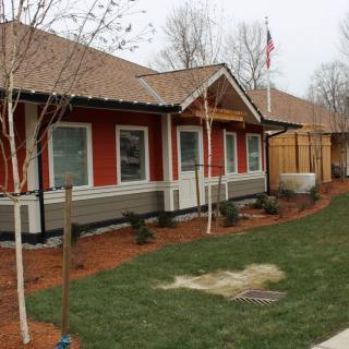 A modern house with a well-maintained lawn and trees, featuring an American flag in the background.