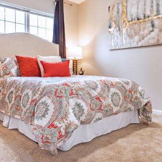 A cozy bedroom with a patterned bedspread, decorative pillows, and wall art.