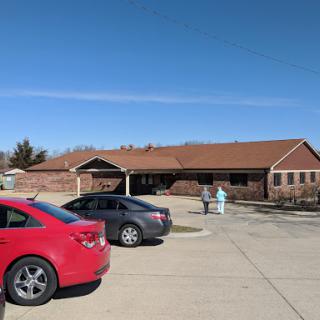 A view of a building from across a parking lot with cars parked nearby under a clear blue sky.