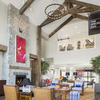 A modern hotel lobby featuring a high ceiling with exposed beams, a cozy fireplace, and stylish furniture.