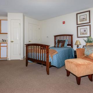 A cozy bedroom with a wooden bed, upholstered chair, and decorative elements.