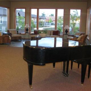 A spacious living room with a grand piano and large windows overlooking a garden.