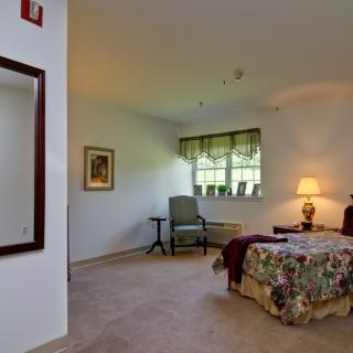A cozy bedroom with a bed, chair, and lamp near a window.