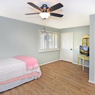 A simple, minimalist bedroom with a single bed, wooden floor, and ceiling fan.