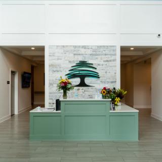 A modern reception area featuring a central desk with floral arrangements and a prominent logo on the wall.