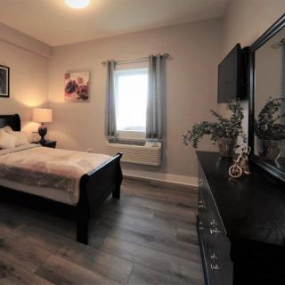 A cozy bedroom featuring a bed, dresser with mirror, and a window with curtains.