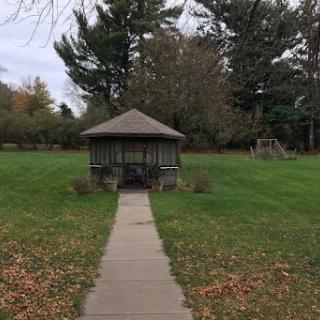 A serene view of a gazebo surrounded by greenery and trees in an autumn setting.