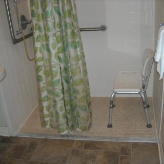 An accessible bathroom with a shower, featuring a safety bar and a chair.