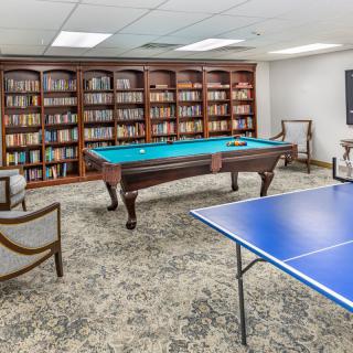 A cozy game room featuring a billiards table, ping pong table, and bookshelves.