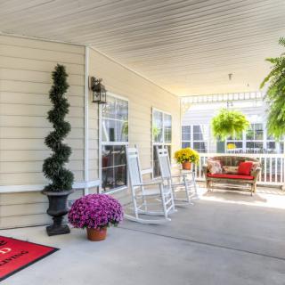 A cozy porch with rocking chairs, a swing bench, and vibrant plants.