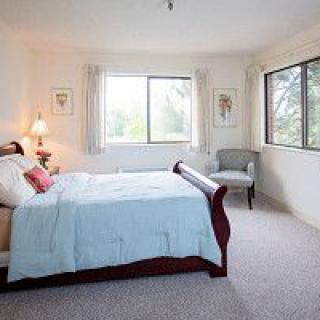 A bright and cozy bedroom with a large bed, windows allowing natural light, and a comfortable chair.