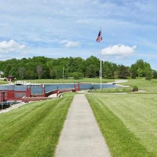 A serene pathway leading towards a picturesque waterfront, adorned with a flag and surrounded by lush greenery.