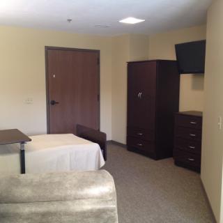 A simple and modestly furnished bedroom with a bed, television, and storage furniture.