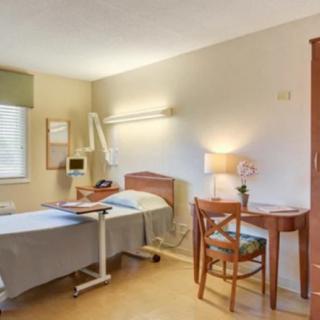 A clean and organized hospital room with a bed, desk, and chair.