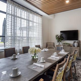 A modern dining room with a large table set for a meeting, featuring elegant decor and natural light from big windows.
