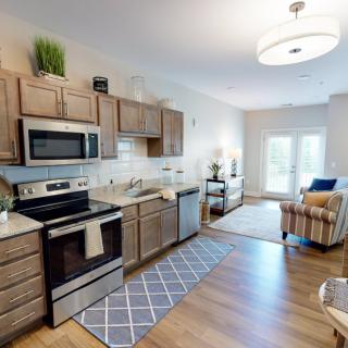 A modern open-concept kitchen with wooden cabinets and stainless steel appliances, leading into a cozy living area.