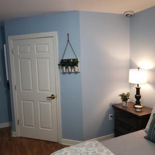 A cozy bedroom with blue walls, featuring a nightstand with a lamp and decorative plants.
