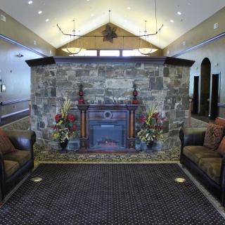 A cozy lobby featuring a stone fireplace, flanked by two comfortable armchairs and illuminated by elegant chandeliers.