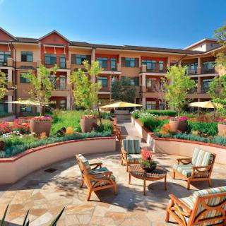 A beautifully landscaped outdoor patio area with chairs and tables, surrounded by a multi-story building.